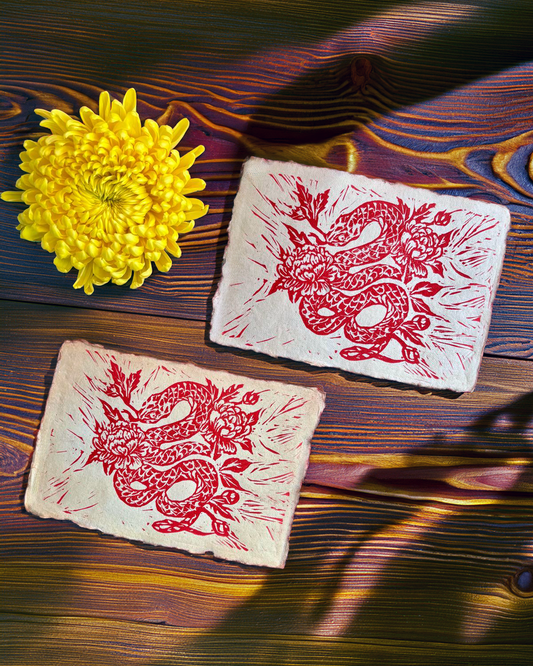 Two square tiles with redsnake designs on a wooden surface with a yellow flower.
