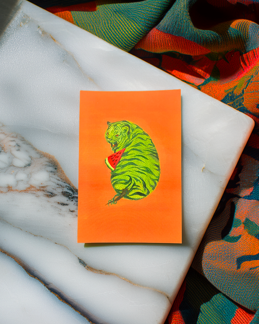 Orange card with a green tiger design on a marble surface with colorful fabric in the background